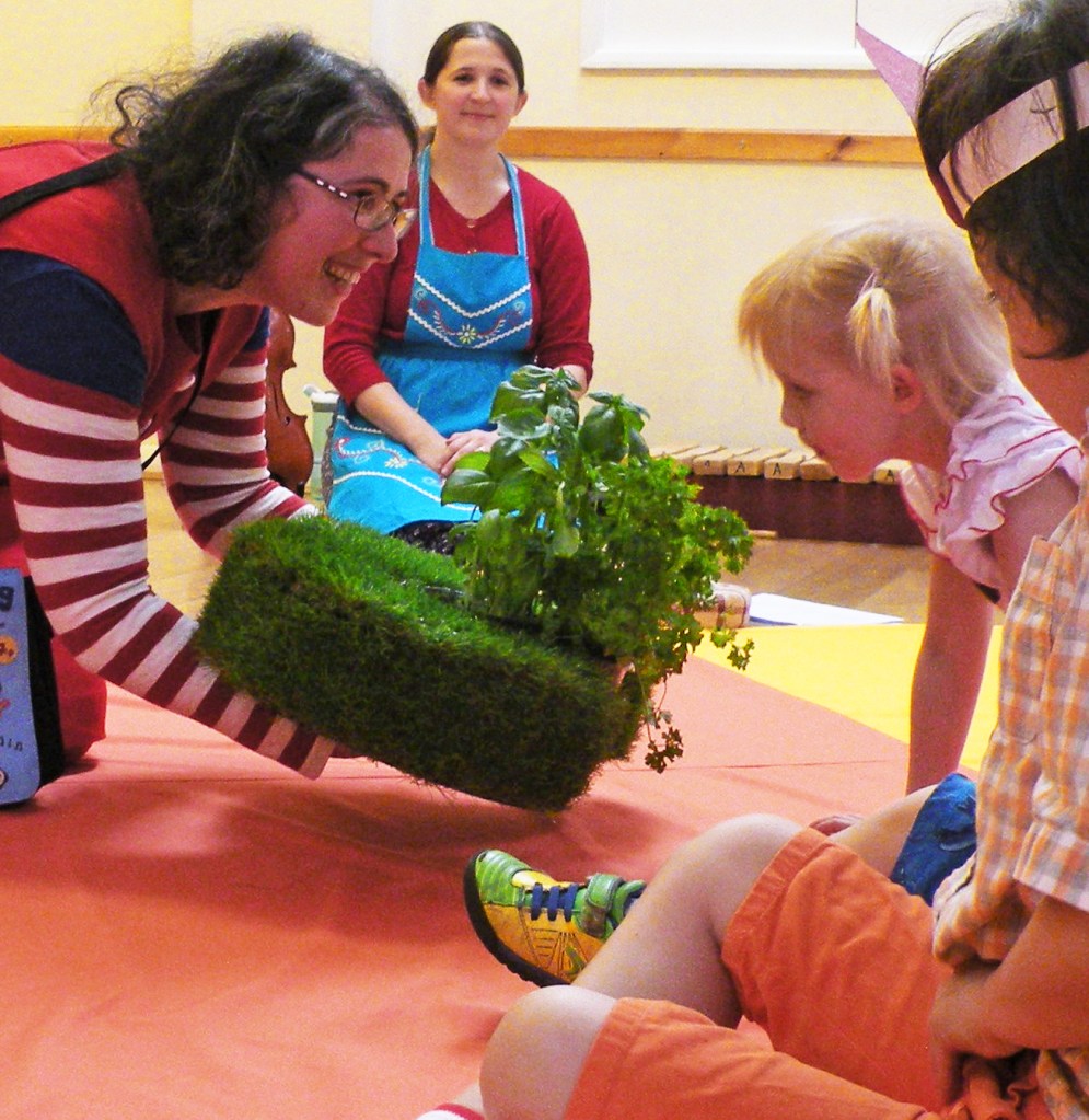 A photo of a small girl sniffing some herbs presented by a performer