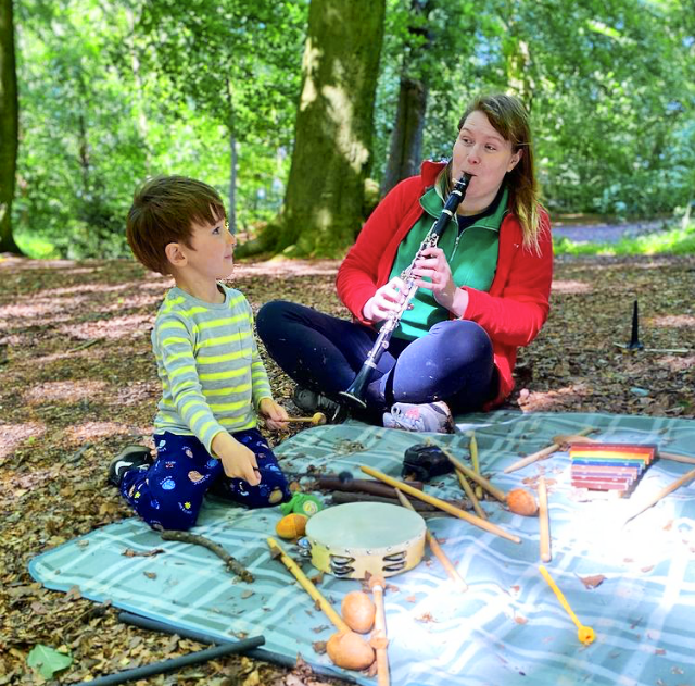 A white musician playing instruments with a small boy in a forest