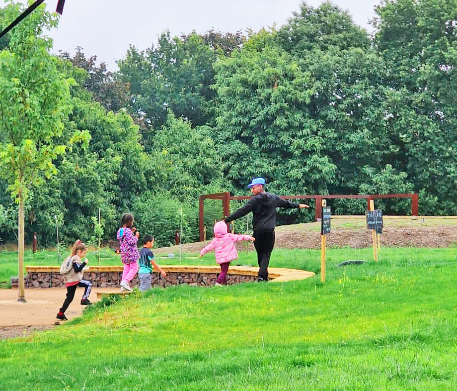 In the distance, a facilitator and a group of children balance on a platform, as they move along it playing a game