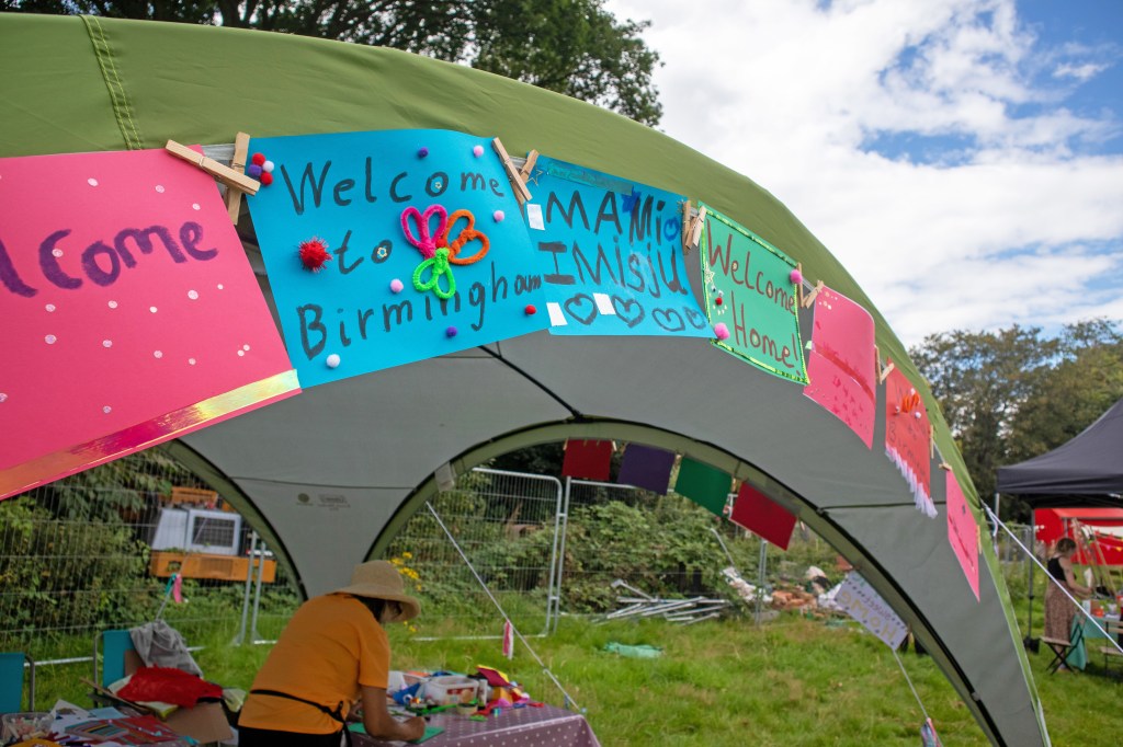 Handmade messages made of coloured paper, pipe cleaners, paint, pompoms and stickers, pegged to a marquee. They say "Welcome", "Welcome to Birmingham", "Mam I mis u", "Welcome Home" and "Welcome Home To Birmingham"